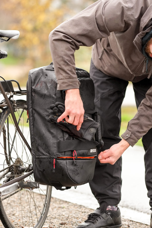 Man biking in the rain with the Two Wheel Gear Duffle bag on the rack of his bike.